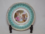 BAVARIA - Prato decorativo em porcelana alemã, borda filetada a ouro com frisos e desenhos de rosas, faixa verde claro, centro aplicado com reprodução de pintura clássica representando cena de serenata. Marcado no fundo. Diâm. 26cm.