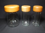 Três potes para mantimentos em vidro, tampa em madeira. Maior com quebrado na borda, porém ainda vedando. Manufatura SY. 20 x 13cm e 20 x 8cm.