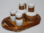 Conjunto galheteiro em porcelana branca sobre bandeja em bambu, trançado e retorcido composto por porta-azeite, porta-vinagre, saleiro e pimenteiro. Uma das garrafas com tampa quebrada. 13 x 27 x 18cm.