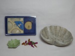 Duas peças: a) Porta-água benta em pedra-sabão esculpida no formato concheado e com volutas. 19 x 16cm. b) Caixa com incensos de fragrâncias domésticas e incensário de porcelana na forma de folha.
