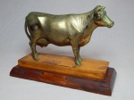 "Vaca leiteira" Escultura em metal amarelo sobre base de madeira. No estado. Alt. total 20cm. Base 26 x 11cm.
