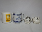 Quatro peças: a) Saleiro e pimenteiro em porcelana branca com listras pretas na forma de gatos. Alt. 6,5cm. b) Duas canecas em porcelana; Metro Design e Sands - Hotel Casino - Las vegas. Alts. 9 e 9,5cm.