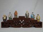 Seis dos 7 Deuses da Felicidade, porcelana japonesa policromada e base de madeira entalhada e vazada formando degraus. Alt. total das peças 6cm. Base 9 x 31 x 5cm.