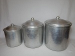 Três potes em alumínio para a guarda de mantimentos. Marcas de uso. Alt. do maior 28cm.