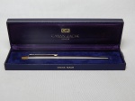 CARAN D'ache - Caneta esferográfica, metal prateado e dourado. Suíça. Embalagem original. Comp. 14cm.