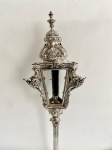 FAUSTOSA LANTERNA PROCESSIONAL SETECENTISTA EM PRATA DE COM ELEGANTE ESTILO DOM JOSÉ I. COM MARCAS PARA CIDADE DE LISBOA (L COROADO) E PRATEIRO AGOSTINHO NUNES DE SOUZA ATIVO NA SEGUNDA METADE DO SEC. XVIII, ATIVO PELO MENOS A PARTIR DE 1770 (MOITINHO, PAG. 100. DECORADA COM ROCAILLES E GUILLOCHES. NAS EXTREMIDADES CAPRICHADAS FOLHAS DE ACANTO. TERÇO SUPERIOR COM FEITIO DE FORMIDÁVEL ABÓBADA QUE FINALISA EM PINHA NO ÁPICE. VARA TAMBÉM EM PRATA DE LEI COM ALMA EM MADEIRA. A GRANDIOSIDADE DESSA LANTERNA PERMITE INFERIR QUE PERTENCEU A PODEROSA IRMANDADE SETECENTISTA. ACOMPANHA BASE DE ÉPOCA EM MADEIRA COM FEITIO TRÍPODE A MANEIRA DE PÉS DE TOCHEIRO. PORTUGAL, SEC. XVIII.  EM MADEIRA REVESTIDA EM VELUDO. BRASIL, SEC. XIX. 57 CM DE ALTURA (SOMENTE AS LANTERNAS). 180 CM DE ALTURA AS LANTERNAS COM AS VARAS. 220 CM DE ALTURA COM A BASE. 4425 G (SEM CONSIDERAR O PESO DA MADEIRA)NOTA: Na Igreja lanternas processionais são usadas em procissões religiosas como Corpus Christi e entradas litúrgicas, geralmente vem antes da cruz processional .Lanternas também são usados para transportar o Fogo Sagrado do Santo Sepulcro no sábado durante a Semana Santa. A procissão religiosa mais célebre a ocorrer no Brasil pelo fausto, riqueza e aparato foi a procissão do triunfo eucarístico as cruzes processionais de fina prata que participaram desse inusitado evento do Brasil Colonial permanecem como registro desse singular evento na sala do Triunfo Eucarístico no Museu da Inconfidência em Ouro Preto. TRIUNFO EUCARÍSTICO: Nos idos de 24 de maio de 1733 realizou-se a solene transladação do Santíssimo Sacramento da Igreja de Nossa Senhora do Rosário para a nova Matriz de Nossa Senhora do Pilar, na antiga Via Rica, hoje Ouro Preto. Nenhum outro acontecimento celebrado em Minas Gerais teve tal esplendor, requinte de luxo e pompa, em plena opulência do ouro. Ele representou grande demonstração do profundo espírito religioso, conjugado a festividades populares, que se observava no Brasil do século XVIII. A comemoração preliminar começou vários dias antes. Desde o final de abril, dois grupos de pessoas ricamente vestidas, com bandeiras de Nossa Senhora do Rosário e de Nossa Senhora do Pilar, tendo na outra face a custódia do Santíssimo Sacramento, percorriam as ruas da cidade e arredores, anunciando a futura solenidade. No dia marcado para a procissão, a cidade amanheceu engalanada. No percurso entre as duas igrejas, as ruas foram atapetadas com flores e folhagens. Como homenagem dos moradores, nas janelas foram colocadas sedas e damascos, em meio a adornos de ouro e prata. Nas ruas, cinco arcos ornamentais, um deles de cera, e um altar para descanso do Santíssimo Sacramento. Antes da saída do cortejo foi celebrada uma Missa, durante a qual o Divino Sacramento esteve colocado em um braço de Nossa Senhora, em lugar do Menino Jesus. Iniciaram a procissão 32 cavaleiros vestidos como cristãos e mouros, com dois carros de músicos instrumentistas e vocalistas. Vinham depois romeiros ricamente trajados, e músicos com alegorias diversas. A seguir, quatro figuras a cavalo, representando os ventos dos pontos cardeais. Todas ricamente revestidas com diamante, ouro, renda, seda e plumas. A comemoração preliminar começou vários dias antes. Desde o final de abril, dois grupos de pessoas ricamente vestidas, com bandeiras de Nossa Senhora do Rosário e de Nossa Senhora do Pilar, tendo na outra face a custódia do Santíssimo Sacramento, percorriam as ruas da cidade e arredores, anunciando a futura solenidade. No dia marcado para a procissão, a cidade amanheceu engalanada. No percurso entre as duas igrejas, as ruas foram atapetadas com flores e folhagens. Como homenagem dos moradores, nas janelas foram colocadas sedas e damascos, em meio a adornos de ouro e prata. Nas ruas, cinco arcos ornamentais, um deles de cera, e um altar para descanso do Santíssimo Sacramento. Antes da saída do cortejo foi celebrada uma Missa, durante a qual o Divino Sacramento esteve colocado em um braço de Nossa Senhora, em lugar do Menino Jesus. Iniciaram a procissão 32 cavaleiros vestidos como cristãos e mouros, com dois carros de músicos instrumentistas e vocalistas. Vinham depois romeiros ricamente trajados, e músicos com alegorias diversas. A seguir, quatro figuras a cavalo, representando os ventos dos pontos cardeais. Todas ricamente revestidas com diamante, ouro, renda, seda e plumas. Seguia-se um personagem representando Ouro Preto, bairro de Vila Rica onde estava situada a Nova Matriz do Pilar, para onde se dirigia o cortejo. Ele trajava vestes de tecidos finos, ornamentados com ouro e diamantes. Seu cavalo era igualmente ajaezado com ouro, prata, esmeraldas e veludo. Vinham depois as esplendorosas figuras representando os corpos celestes: Lua, Marte, Mercúrio, Sol, Júpiter, Vênus e Saturno, todas com deslumbrantes indumentárias e fartamente escoltados. A seguir aparecia a figura que representava a Igreja Matriz do Pilar, com exuberantes ornamentos, portando um estandarte com a inscrição Nossa Senhora do Pilar em um dos lados, do outro o desenho da custódia eucarística. Após essas figuras, sumariamente descritas, vinham as irmandades, conduzindo andores com seus santos padroeiros e cruzes de prata. Entre essas confrarias estavam as do Santíssimo Sacramento, de Nossa Senhora do Rosário, de Santo Antonio, de Nossa Senhora da Conceição e de Nossa Senhora do Pilar. Todos os participantes portavam trajes esplendorosos com acabamento em veludo e seda, ouro, prata e pedrarias. Fechando a procissão, o Santíssimo Sacramento, conduzido pelo vigário da Matriz do Pilar, debaixo de um pálio de tela carmesim com ramos e franjas de ouro, sustentados por seis varas de prata. Logo atrás o Conde de Galvêas, Governador de Minas Gerais, com autoridades civis e militares da Província e do Município. Com toda a população de Ouro Preto e arredores presente, foi uma grande apoteose: sinos tocando, bandas musicais, fogos e cânticos em homenagem ao Santíssimo Sacramento. Os festejos prolongaram-se por três dias, com Missas solenes, cavalhadas, corrida de touros e fogos de artifício. O Triunfo Eucarístico foi sem dúvida a maior festa barroca de todos os tempos e um dos eventos religiosos e sociais mais exuberantes da América Portuguesa. Em seu livro O Triunfo Eucarístico Exemplar da Cristandade Lusitana, publicado em 1734, Simão Ferreira Machado, português residente em Minas Gerais, se refere aos seus compatriotas como sendo os senhores dos mais finos diamantes de todo o mundo, em um momento ao qual referiu não ter tido lembrança que visse no Brasil, nem consta, que se visse na América ato de maior grandeza. Na Minas Gerais barroca, um Brasil autêntico que infelizmente se foi Mas nessas fulgurações da nacionalidade encontra-se a luz que ainda pode nos indicar o caminho a retomar com vistas ao futuro. Luz que brilha na constelação do Cruzeiro do Sul. Luz que se chama Civilização Cristã.( O triunfo eucarístico em Minas Gerais Por Carlos Sodré Lanna)