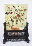 TABLE SCREEN EM JADE COM APLICAÇÃO DE PEDRA DURA, AMETISTA E LAPIS LAZULI - PRECIOSO TABLE SCREEN / BIOMBO DE MESA EM JADE COM INSCRUSTAÇÃO DE PEDRA DURA, AMETISTA E LAPIS LAZULI. OBJETO DE ALTO LUXO NA CULTURA ORIENTAL CONSTRUÍDO COM INIGUALÁVEL QUALIDADE E REQUINTE. TRATA-SE DE PEÇA PALACIANA! CONSTRUÍDO COM UMA FINA CAMADA EM JADE DECORADA COM INSCRUSTAÇÃO DE PEDRA DURA E LAPIS LAZULI FORMANDO GROU COM RAMAGENS E FLORES. A PLACA É ENCAIXADA EM SUPORTE ASSENTE SOBRE QUATRO PÉS, PROFUSAMENTE ENTALHADO E DECORADO COM APLICAÇÃO DE MEDALHÕES EM AMETISTA E PEDRA DURA.  CHINA, DINASTIA QIAN REINADO DAOGUANG, CIRCA DE 1850. 32 X 22 CM (MINIMAS FALHAS NA INCRUSTAÇÃO) NOTA: Biombos de mesa antigos, são decorados com símbolos importantes e auspiciosos, eram um dos objetos mais importantes no atelier de um estudioso antes da dinastia Qing na China e da mesma forma no Japão. Um biombo de mesa era colocado sobre a mesa de trabalho de um estudioso onde desenvolvia suas escritas em frente a uma janela assim o pequeno biombo protegia o papel da brisa e evitava acidentes como manchar a escrita. Mais tarde, eles eram objetos de valor em casas abastadas, e hoje os colecionadores os desejam por seu virtuosismo e elegância. Nas dinastias Ming (1368/1644) e Qing (1644/1911), um biombo de mesa de jade, geralmente decorado em ambos os lados e apoiado em um suporte de madeira, passou a representar o auge da moda entre a elite educada da China. .Um biombo de mesa de jade branco que compõe o acervo do Museu de São Francisco é decorado de um lado com imagens de tesouros favorecidos pelos estudiosos, enquanto o verso mostra três homens idosos viajando entre templos de vários andares em altas montanhas. No Museu de Belas Artes de Houston, um biombo de mesa da dinastia Ming exibe entalhes decorativos em ambas as superfícies.De um lado, um qilin - uma fera mítica semelhante a um unicórnio - se põe contra uma paisagem rochosa.O outro lado apresenta dignitários da corte que perseguem várias atividades acadêmicas. Outros biombos de mesa foram adornadas com imagens como lótus (simbolizando pureza), dragões (força ou poder e boa sorte) ou nuvens (boa sorte). Os biombos de mesa foram usados principalmente para 'inspiração e contemplação. O biombo inspirava tranquilidade e paz, além de benevolência. Enquanto você compunha poesia ou música, ou se escreviam textos,  olhava para o biombo, isso inspirava ou ou trazia tranquilidade.