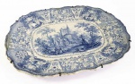 ADAMS DELPHI BLUE  LINDA TRAVESSA EM PORCELANA DECORADA EM AZUL. MARCAS DA MANUFATURA ADAMS PADRÃO DELPHI. BORDA RECORTADA COM ABA CONTENDO EXUBERANTE DECORAÇÃO DE FLORES E RAMAGENS. CALDEIRA COM RESERVA COM CASTELO EM RUÍNAS, UMA CRUZ DE CRUZEIRO E UM CASAL COM TRAJES DO SEC. XIX COM UM CÃO E UM PERSONAGEM SENTADO AO CHÃO COM TURBANTE INDIANO. ADAMS & SONS FORAM OLEIROS PROLÍFICOS E OPERARAM DE 1800-1864. O DESENHO DESTE PRATO PODE SER VISTO EM "ROMANTIC STAFFORDSHIRE CERAMICS" DE JEFFREY B. SNYDER NA PÁGINA 18. INGLATERRA, SEC. XIX. 44 CM DE COMPRIMENTO. (restauro profissional na borda provavelmente uma antiga esbeiçadela porque a travessa não tem som de louça restaurada)