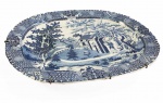 LINDA TRAVESSA EM FAIANÇA DECORADA COM PAISAGEM ORIENTAL. BELISSIMO EXEMPLAR DA PRIMEIRA METADE DO SEC. XIX. APRESENTA CONCAVIDADE E ESTRIAS PARA CONDUÇÃO E ARMAZENAMENTO DE CALDOS DE ASSADOS. INGLATERRA, INICIO DO SEC. XIX. 40 CM DE COMPRIMENTO