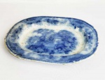 FLOW BLUE  BELA TRAVESSA EM FAIANÇA DITA BORRÃO. DECORAÇÃO EM AZUL COM VEGETAÇÃO E PAGODES. INGLATERRA, PRIMEIRA METADE DO SEC. XIX. 28 CM DE COMPRIMENTONOTA: A louça borrão foi produto de experiência dos fabricantes ingleses que na primeira metade do sec. XIX iniciaram tentativas para decorar a porcelana com cobalto, técnica milenar desenvolvida pelos chineses. Nas primeiras décadas a técnica, ainda não dominada totalmente, produzia louça com bela tonalidade azul cobalto, mas sem definição precisa da decoração. Daí o nome borrão. Como não tiveram boa aceitação nos mercados europeus eram enviadas como lastro nos navios para serem comercializadas nas colônias da América. Essa é a louça primitiva utilizada no Brasil pelas famílias abastadas e bastante colecionada nos dias atuais por ter sua raridade e beleza.