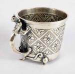 LUIZ FERREIRA GRANDE CANECA EM PRATA DE LEI DECORADA COM LOZANGOS CONTENDO CRUZES LATINAS EM RELEVO. PEGA COM FEITIO DE SALAMANDRA. ESTILO E ÉPOCA ART DECO.. MARCAS DE CONTRASTE ÁGUIA PRIMEIRO TÍTULO, PARA CIDADE DO PORTO E CHANCELA DO ARTISTA. PORTUGAL, 11 X 10 CM. 405 GNOTA: Luiz Ferreira nasceu numa família de ourives. Nos dizeres de Gonçalo Vasconcelos e Sousa ele "bebeu na tradição portuense de formar dinastias de ourives, de casar entre famílias profissionais do mesmo ofício". Os seus avós, paterno e materno, respectivamente David Ferreira (Porto) e Luís António Monteiro (Tondela), eram ambos mestres ourives. Do pai, também David Ferreira, herdou a oficina e loja na Rua das Flores, depois transferida para a Rua de Trindade Coelho, onde ainda hoje se acumulam coleções das suas peças. Os "bichos" de Luiz Ferreira estão representados em vários museus nacionais e estrangeiros. E, ao longo das décadas do século XX, levaram o nome da ourivesaria - e a marca "LF" - aos acervos de figuras do mundo inteiro, desde a rainha de Inglaterra ao rei Juan Carlos de Espanha, do Presidente americano Ronald Reagan à primeira-dama Jacqueline Kennedy, mas também às coleções das casas Dior, Chanel, Tiffany"s e Cartier.