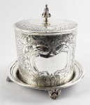 PRATA DE LEI INGLESA - ELKINGTON  FORMIDÁVEL BISCOITEIRA EM PRATA DE LEI INGLESA. MARCAS DE CONTRASTE PARA CIDADE DE BIRMINGHAM E PRATEIRO ELKINGTON PRATEIRO OFICIAL DA RAINHA VITORIA E SOBERANOS SEGUINTES ATÉ OS DIAS DE HOJE. LINDA E ROBUSTA PEÇA, DECORADA COM ELEMENTOS FLORAIS AO GOSTO VITORIANO. TAMPA BASCULANTE. ASSENTE SOBRE QUATRO PÉS VAZADOS. INGLATERRA, INICIO DO SEC. XX. 18 X 18 CM. 1020 GNOTA: A manufatura ELKINGTON foi fundada por George Richards Elkington e seu irmão, Henry Elkington, na década de 1830. Ela operou sob o nome de GR Elkington & Co. até 1842, quando um terceiro sócio, Josiah Mason, ingressou na empresa. Operou como Elkington, Mason, & Co. até 1861, quando a parceria com a Mason foi encerrada. A empresa operou independentemente como Elkington & Co. de 1861 até 1963. Foi então adquirida pela British Silverware, Ltd .. Em 1971, a British Silverware, Ltd. tornou-se uma subsidiária da Delta Metal Co. Ltd.  Ao longo da história, tornou-se um grande sucesso e recebeu vários mandados reais de nomeações e também um Mandado Imperial e Real de nomeação do imperador da Áustria. Uma de suas obras mais famosas é réplica do Jerningham Wine Cooler que integra o acervo do Victoria & Albert Museum .
