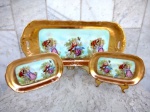 Conjunto de grande Travessa retangular em porcelana PA , original da década de 50 e duas travessas menores , também retangulares , esmaltadas , decoradas com espessas coberturas em ouro brunido , tendo ao centro cenas galantes em paisagens idílicas em rica policromia. Medidas 44 x 20 cm e 19 x 12 cm .