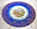 DP : Lindo Medalhão em porcelana no tom azul rei degradée com arabescos em ouro e ao centro pintura com rica policromia  de cena de damas e cavalheiro em jardim paradisíacos . Diâmetro 24 cm.