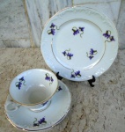 Trio de Xícara de chá com pires e prato para bolo em porcelana esmaltada branca e vitrificada com  suaves ramos de delicadas flores lilás . Bordas com chanfrados em alto relevo e frisos em ouro. 18 /15 / 8 de altura , porcelana de STA CATARINA Schmidt
