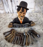 Porta chaves para se colocar na parede em resina com a figura de Charlie Chaplin e dezessete chaves antigas envoltas num aro de metal medindo 15 cm de altura por 14 cm de comprimento.