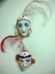 Duas máscaras em Faiança para parede , estilo venezianas , com plumas e medindo 18 x 12 cm.
