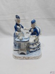 Escultura em porcelana azul e branco, retratando damas antigas. Medindo 22,5cm de altura. Leve restauro no pé da mesa.