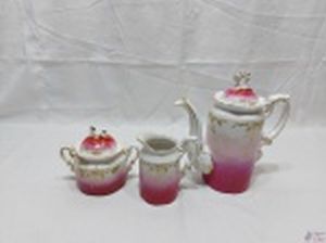 Jogo de servir café em porcelana europeia com detalhes ouro e relevo. Medindo o bule 21,5cm de altura. O bule possui um bicado na borda, o açucareiro uma perda na alça da tampa e a leiteira com um bicado na ponta.