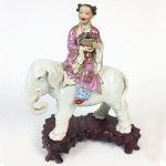 Escultura em porcelana policromada representando figura feminina oriental sobre elefante. Marcas no verso. Acompanha base em madeira. China, Princípio do Séc. XX.  28 cm de altura sem a base e 32 cm de altura com a base. (Devido a fragilidade desse lote, seu envio só será realizado através de transportadora especializada).