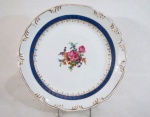 SCHMIDT-  Grande medalhão em porcelana branca, decorada ao centro com flores, borda com largo friso azul e guirlandas em dourado. Med. 32 cm diâmetro.