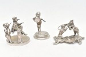 Três esculturas de metal prateado representando a primeira 2 meninos fumando , o segundo menino com cartola e corpo de noz moscada, o terceiro cena circense de palhaço e cão. Altura maior 10,5 cm.