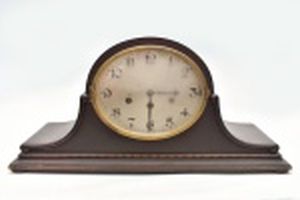 Relógio de lareira alemão com soneria a quartos de hora, tendo 4 martelos, 3 furos para corda e pêndulo, caixa em madeira escura, vidro da frente bombê com opacidade, mostrador metálico. Frente 54 cm. altura 25 cm.