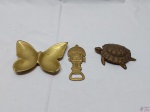 Lote composto de cinzeiro na forma de tartaruga, petisqueira na forma de borboleta e abridor de garrafa na forma de totem em bronze. Medindo a boboleta 14cm x 11cm.