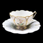 PORCELANA - Bela xícara de chá em fina porcelana branca, pintada a mão com seu respectivo pires. Med. 5x8 cm e 14 cm. Marcas do tempo e fios de cabelo.