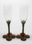 DEMI CRISTAL -  Par de fluts em demi cristal, bojo incolor, haste em metal trabalhado e base com aplicações em gotas em tom âmbar.