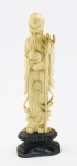 MARFIM - Bela escultura oriental chinesa em marfim, representando o Ímortal Shou Xing, em pé segurando seu cajado e no colo pêssego. Alt. 18 cm. Base em madeira.