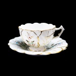 PORCELANA - Bela xícara de chá em fina porcelana branca, pintada a mão com seu respectivo pires. Med. 5x8 cm e 14 cm. Marcas do tempo e fios de cabelo.