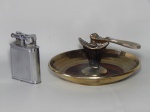 Duas (2) peças: a) Antigo isqueiro a querosene "Lift arm" Dunhill, confeccionado em metal prateado, patente nº 143752. 11 x 8cm. b) Quebra-nozes de mesa em material sintético e metal.  12 x 20cm.