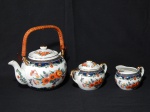 Três (3) peças em porcelana branca, bule, açucareiro e cremeira, decoradas por arranjos florais em policromia e douração, bule com alça em palha. Alts. 20, 9 e 7cm.