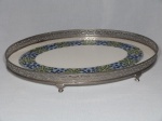 Bandeja austríaca, oval, estrutura de metal prateado, fundo de louça com faixa estampada com folhagens. Pés e galerias vazados em metal prateado. Marcada no fundo. 34 x 43cm.