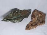 Duas peças: a) Escultura em metal amarelo moldado na forma de folha, apresenta desgastes. 37 x 15cm. b) Saboneteira em pedra esculpida e polida. 30 x 21cm.