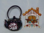 Duas peças: a) Bule em cloisonné chinês, fundo azul cobalto decorado com flores policromadas. Alt. 15 cm b) Um porta chaves em porcelana branca moldada na forma de casa pintado à mão, souvenir da cidade de gramado. Alt. 14cm