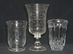 Três peças: a) Vaso em cristal translúcido moldado com sulcos facetados. Alt. 16cm. b) Dois vasos em demi-cristal, sutil lapidação de folhagens. Alt. 25cm e 16cm.