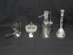 Quatro peças para laboratório em vidro translúcido, sendo 1 condensador Graham (apresenta quebrados), 1 kitassato, 1 balão volumétrico e um pote com vedação. Alt. 15cm, 8cm, 15cm e 9cm.