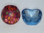 Duas (2) peças em vidro: porta-velas esférico, revestido por estampa florida sobre fundo magenta, alt. 10cm; e cinzeiro em grosso vidro azul. 6 x 12 x 12cm.