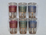 Seis copinhos em vidro translúcido decorado em diferentes cores e aplicado com faixas, volutas e folhagens em douração. Alt. 8cm