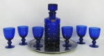 Conjunto de licoreiro com 6 taças em vidro no tom azul cobalto. Licoreiro decorado com sulcos em relevo. Acompanha bandeja circular em metal prateado. Alt. licoreiro 24 cm.