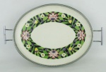 Bandeja ovalada, de coleção, em faiança europeia, decorada ao centro com flores em policromia. Guarnições em metal prateado. Peça numerada em crivo. Med. 34,5x37,5x23,5 cm.