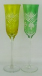 Par de taças de pé alto em cristal, sendo uma na tonalidade translúcida e verde, e a outra translúcida e amarela. Lapidações dedão, sulcos, olivas e folhas. Alt. 24 cm.