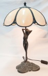 Bela luminária de mesa italiana, estilo Art-noveau, em bronze patinado na forma de Nú feminino. Cúpula ao estilo Tyfany em baquelite. Base em metal com trabalhos de flores e folhas. Metal com marcas do tempo. Funcionando. Alt. 52 cm.