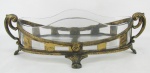 Centro de mesa em pewter americano patinado de dourado, com marca da manufatura Wallace Bros Silver Co., decorado com folhagens, geométricos, volutas e vazados. Recipiente em viro translúcido, com 2 bicados na borda. Pewter com pequenos desgastes causados pelo tempo. Med. 12,5x41,5x20cm.