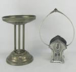 WMF - Duas peças alemães em metal, com marca da manufatura, sendo base para centro de mesa e base para floreira na forma de cesta, ambas decoradas com trabalhos em relevo. Faltam os vidros e marcas de uso. Alts. 21,5 e 25,5cm.