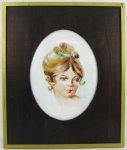 Placa oval em porcelana, com pintura policromada de busto de menina. Emoldurada. Med. placa 23,5x18cm e Med. moldura 38x32cm.
