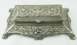 Porta selos em metal espessurado a prata, contendo 5 compartimentos. Decorado com trabalhos de vasos com flores, folhagens e volutas em relevo. Med. 6x21,5x13cm.