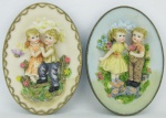 Duas placas em resina policromada, decoradas com cenas de casal de crianças no jardim em alto relevo. Med. 19,5x14 e 19x14 cm.